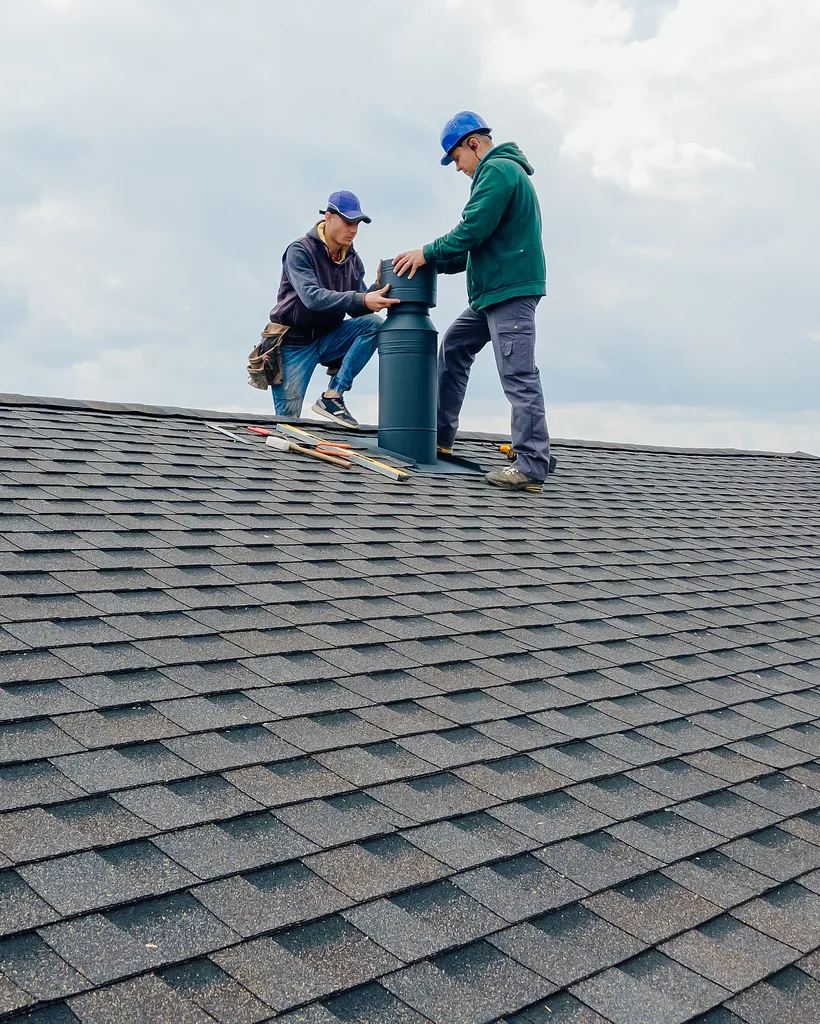 roofing crew installing a chimney flue on an asphalt shingle roof